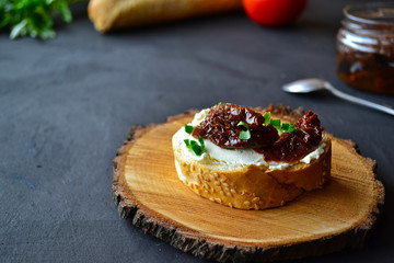 French baguette with cream cheese and dried tomatoes on a dark background.