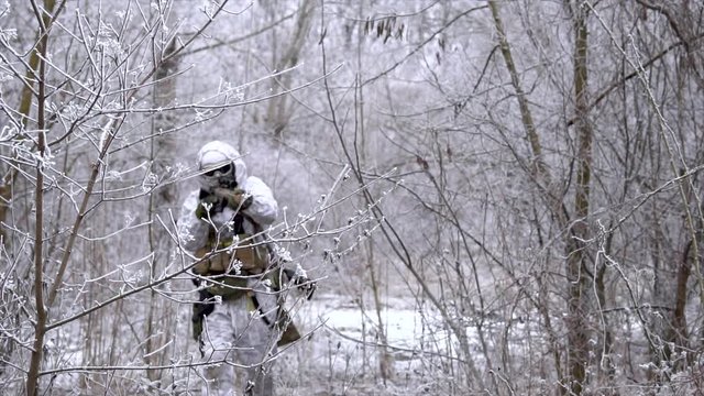 Two military men in white camouflage and green uniform, in winter forest. Soldiers with machinegun join and sneaking front view.