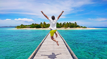 Excited happy traveling young man jumping with joy on the pier on beautiful Mala Mala Island, Fiji, Pacific Ocean.
