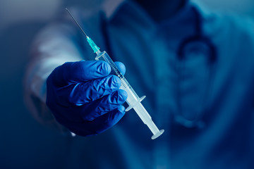 doctor sosteniendo una jeringuilla en la mano con guantes azules y fondo oscuro