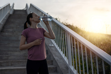 Picture of fitness girl drinking water, taking rest from training. Fitness women training and doing workout outdoors in city.