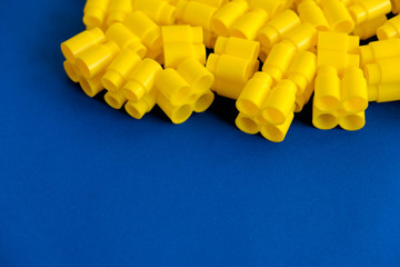 Yellow plastic building blocks on a blue background. Pieces and elements of constructor. Parts of...