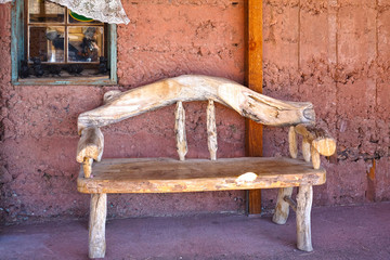 Single rustic bench made of untreated wooden logs in front of a house