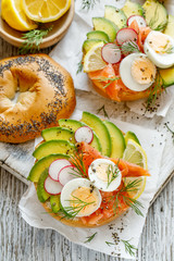 Bagel sandwich with smoked salmon,  avocado boiled eggs radish lemon and fresh dill, top view. Delicious and healthy breakfast
