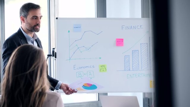 Video of handsome businessman explaining a project with whiteboard to his colleagues on coworking place.