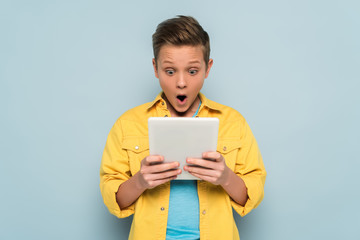 Obraz premium shocked kid using and looking at digital tablet on blue background
