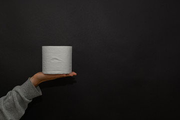 Female hand holds a roll of toilet paper on the palm. Trend, panic, lack of goods. Virus, epidemic, quarantine. Copy space. Dark background.