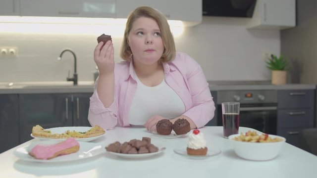 Young fatty woman hiccupping while eating sweet dessert at home, sugar overdose