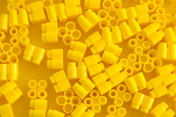 Yellow plastic building blocks on yellow background. Background of plastic details building blocks. Parts of bright small spare parts for toys. Top view. Copy, empty space for text