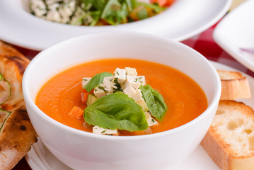 Pumpkin soup with feta cheese and vegetables served in white bowl topped with spinach with other Italian dishes