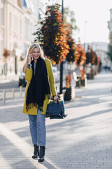 Fototapeta premium cute attractive blonde woman with packages on the street in sunny weather. communicates on the phone after shopping, positive emotions.