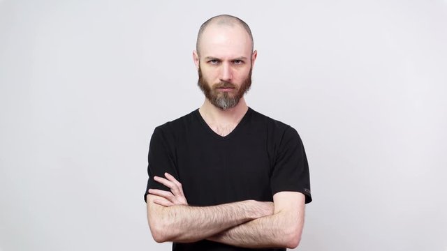 Strict bearded man looking at a camera over white background. Serious dissatisfied man keeps hands crossed. Concept of emotions.
