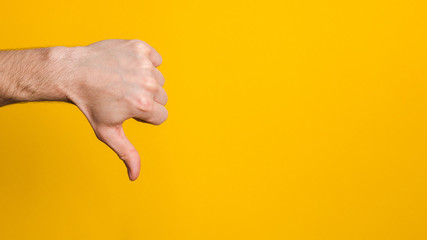dislike sign. man hand with thumb down over yellow background with copy space
