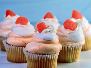 Vanilla cupcakes with orange and white swirled frosting and an orange candy gumdrop on top, festive and delicious for a celebration with a sandstone background.