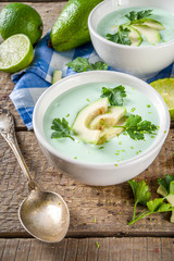 Homemade avocado cream soup with lime, herbs and avocado slices on wooden rustic background, copy space