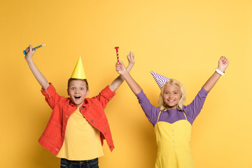 smiling kids with outstretched hands holding party horns on yellow background