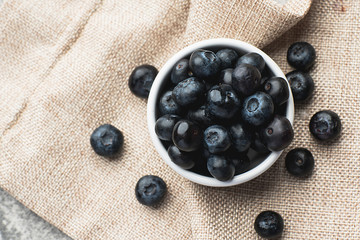 Fresh heap of blueberry in white clean bowl on sack cloth.