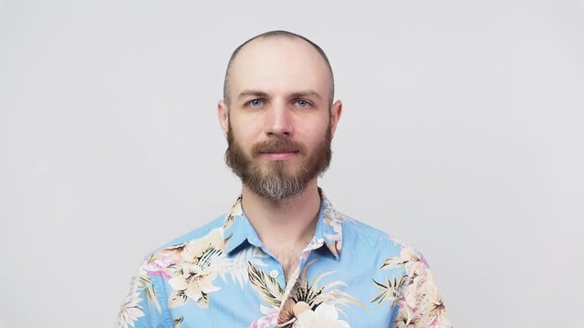 Portrait of calm bearded man looking at camera wearing hawaiian shirt, isolated over white background. Concept of emotions.