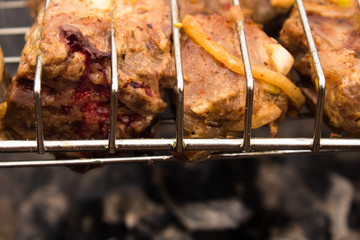 Barbecue of pork with blood on the grill in the process of cooking on an open fire. A piece of pork on the grill with blood juice protruding from it, close-up.