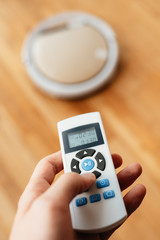 A remote control controls a robotic vacuum cleaner on the wooden floor