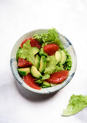 Avocado grapefruit salad with lettuce in a bowl on grey metal background. Raw vegetarian detox salad, healthy food. Selective focus