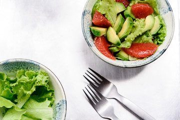 Avocado grapefruit salad with lettuce in a bowl on grey metal background. Raw vegetarian detox salad, healthy food. Selective focus