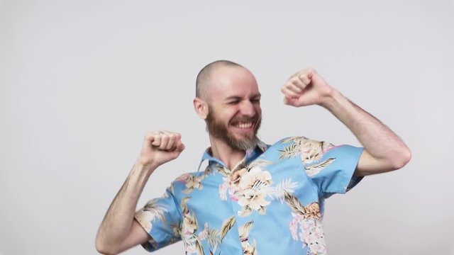Happy man wearing hawaiian shirt celebrating a victory over white background, slow motion. Emotions of success, triumph, victory, winning and celebration.