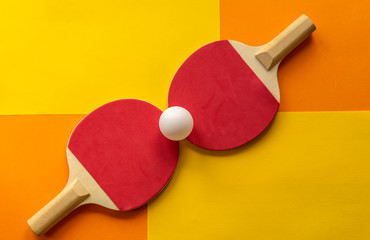 Table tennis rackets and white tennis ball lie on a bright multicolored background