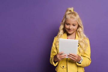 smiling kid using digital tablet on purple background with copy space