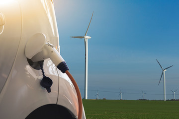 Electric car with charging plug on a background of wind turbines