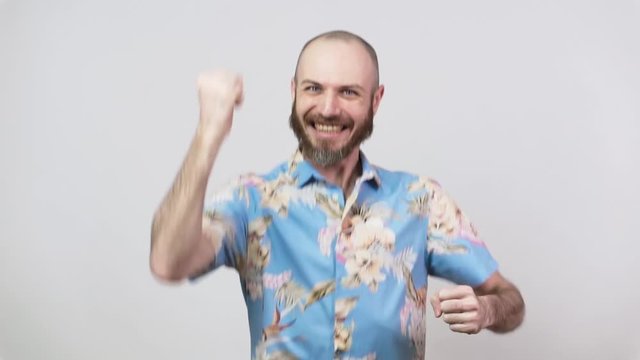 Amazed happy man wearing hawaiian shirt celebrating a victory over white background, slow motion. Emotions of success, triumph, victory, winning and celebration.