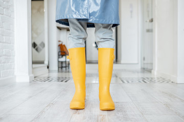 Woman in yellow rubber boots and raincoat standing in the corridor at home, ready to walk outside in rainy weather