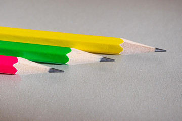Pink, yellow and green graphite pencils on a gray background close-up.
