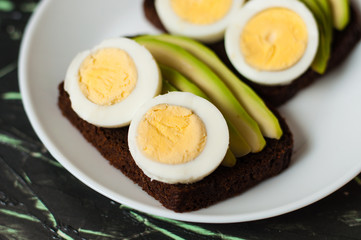 Sandwiches with brown bread, avocado and egg on a dark background, top view