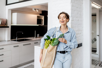 Portrait of a young and cheerful woman standing with shopping bag full of fresh vegetables and...