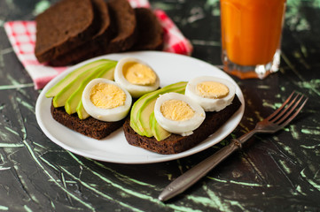 Black whole grain bread, sandwiches with eggs and avocados, multifruit juice in a tall glass. Concept proper nutrition
