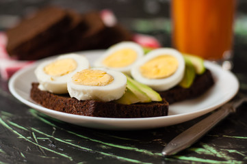 Black whole grain bread, sandwiches with eggs and avocados, multifruit juice in a tall glass. Concept proper nutrition