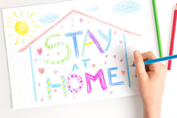 Quarantine at home during coronavirus pandemic. Kid hand drawing with coloring pencils picture with words Stay at home. Social media campaign for coronavirus prevention