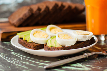 Black whole grain bread, sandwiches with eggs and avocados, multifruit juice in a tall glass. Concept proper nutrition