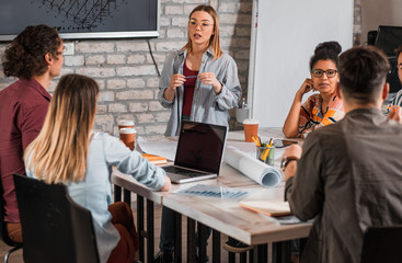 Group of modern business people in casual wear discussing architectural designs while sitting in the creative office.