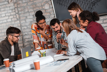 Group of modern business people in casual wear discussing architectural designs while sitting in the creative office.