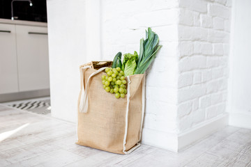 Shopping bag full of fresh vegetables and greens on the white wall background indoors