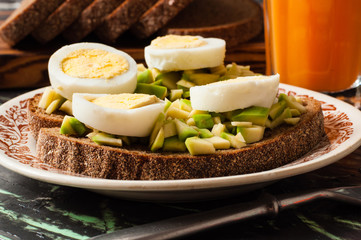 A glass of juice, sandwiches with avocado and egg, black whole grain bread. The concept of diet and proper nutrition