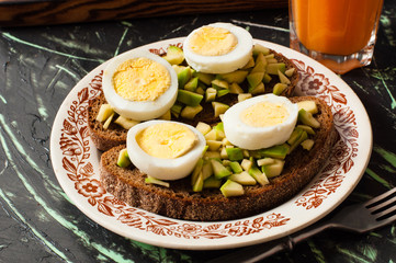 A glass of juice, sandwiches with avocado and egg, black whole grain bread. The concept of diet and proper nutrition