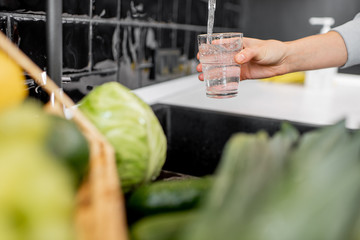 Woman filling drinking glass with tap water on the kitchen. Concept of clean drinking tap water at home