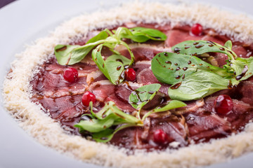 veal carpaccio on a white plate with grated parmesan cheese with basil 
