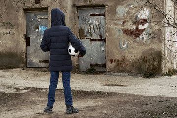 concept of epidemic and quarantine - a boy with a face mask and a ball alone on the street in the city