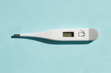 One plastic white electronic thermometer with shadows isolated on sunny light blue background. Health care treatment concept
