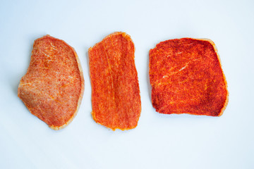 Dried slices of pork, beef of different shapes with spices on a white background. Crispy meat chips. Tasty appetizer. View from above.