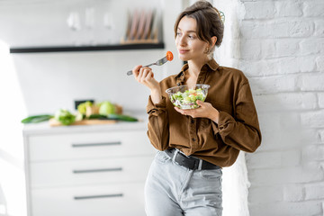 Portrait of a young and cheerful woman eating healthy salad on the kitchen at home. Healthy eating, wellbeing and lifestyle concept